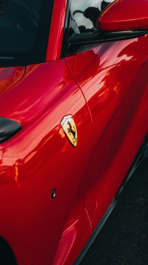Gros plan d’une voiture de luxe rouge brillant avec écusson cheval cabré sur l’aile, reflet urbain sur la carrosserie